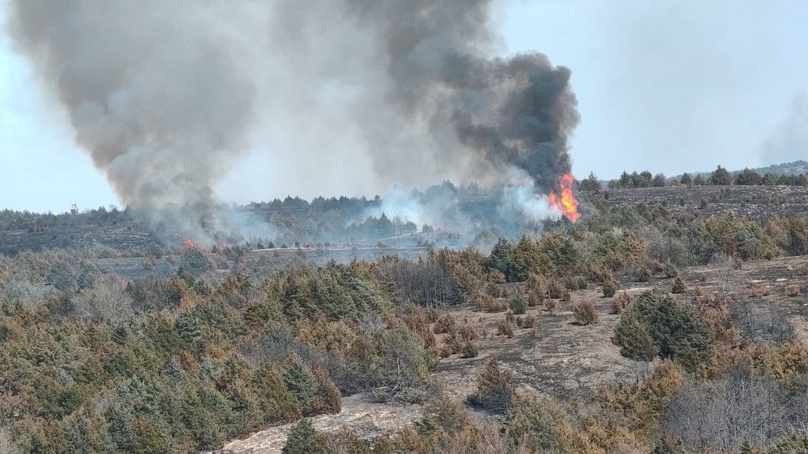 Smoke and flames rising from a brush fire across open rangeland